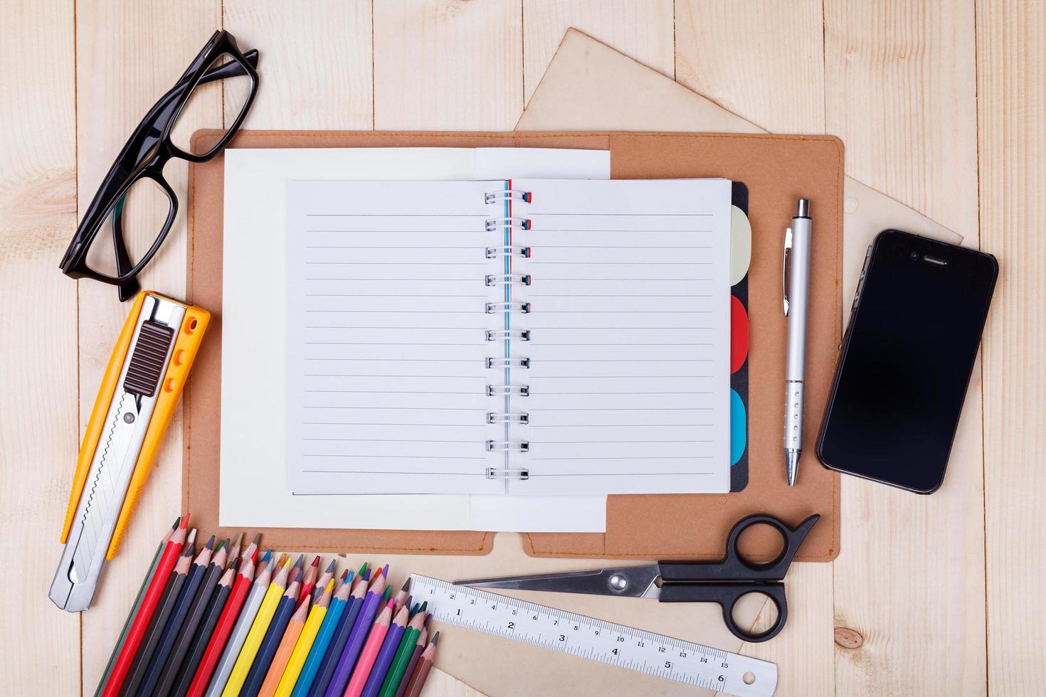 Workplace with colored pencils and supplies, notebook, eyeglass on wooden table photo