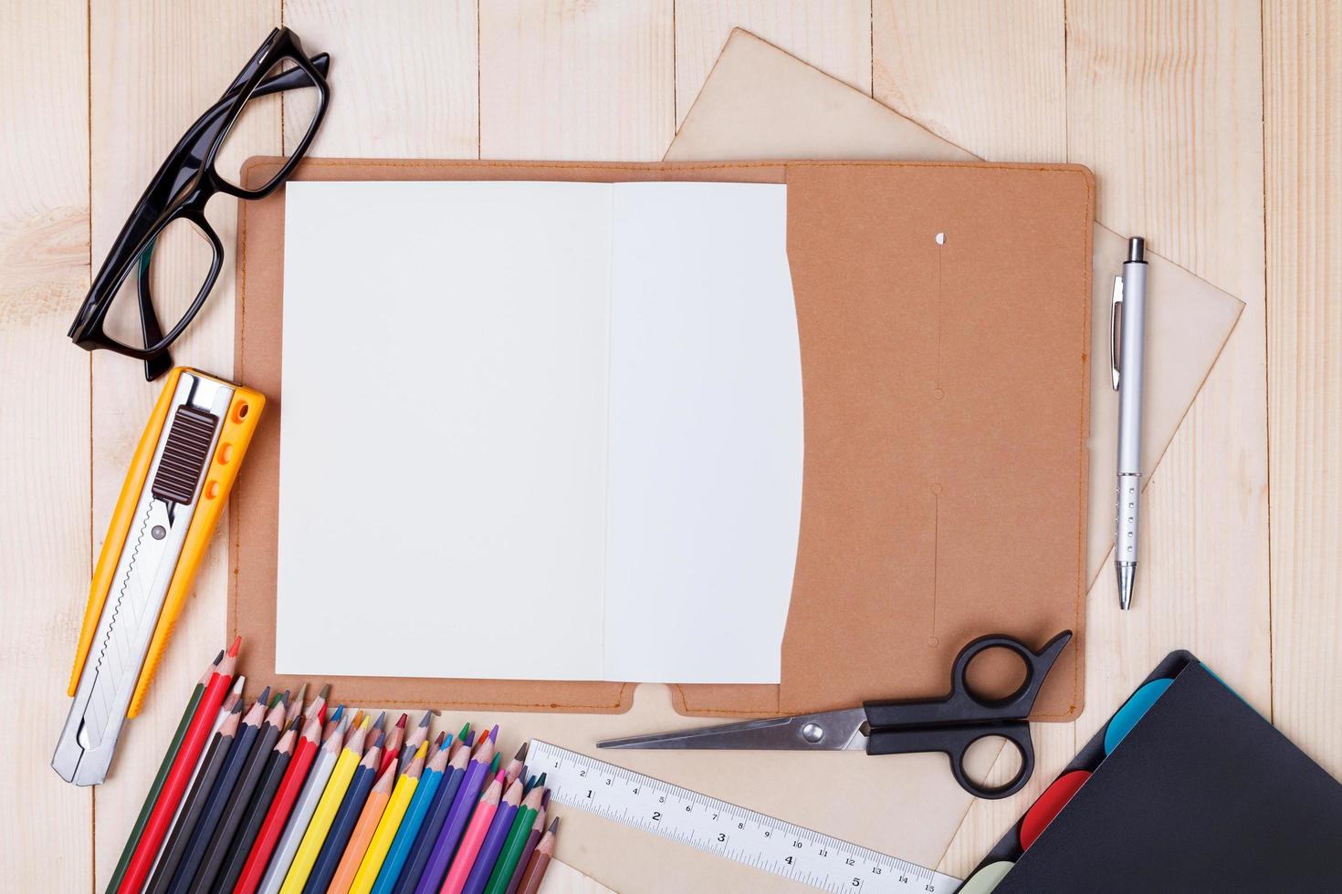 Workplace with colored pencils and supplies, notebook, eyeglass on wooden table photo