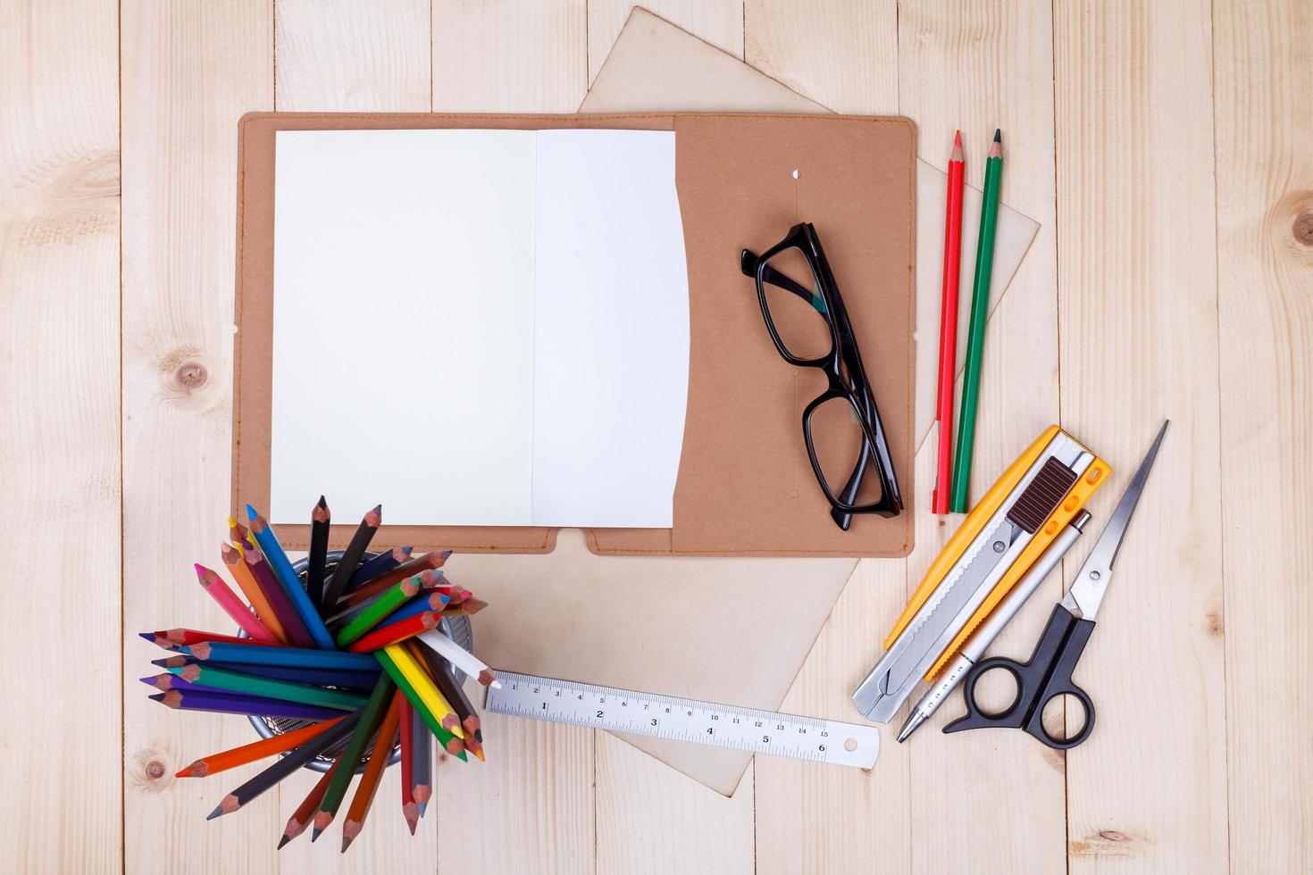 lugar de trabajo con lápices de colores y suministros, cuaderno, anteojos en mesa de madera foto