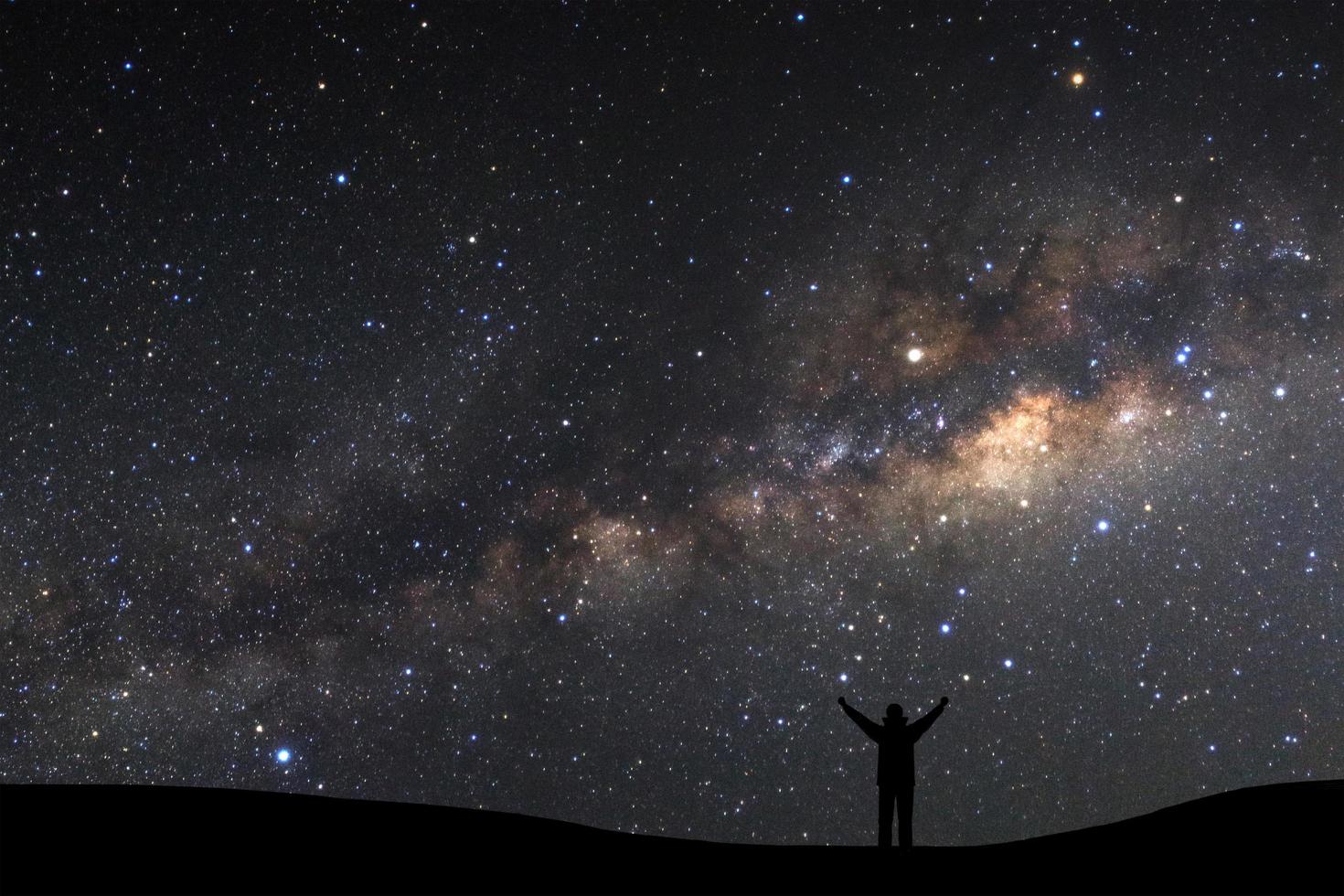 landscape with milky way, Night sky with stars and silhouette of a standing sporty man with raised up arms on high mountain. photo