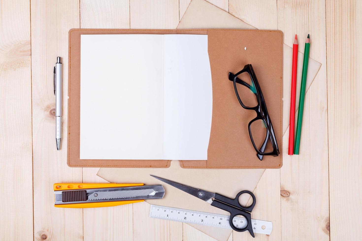 Workplace with colored pencils and supplies, notebook, eyeglass on wooden table photo