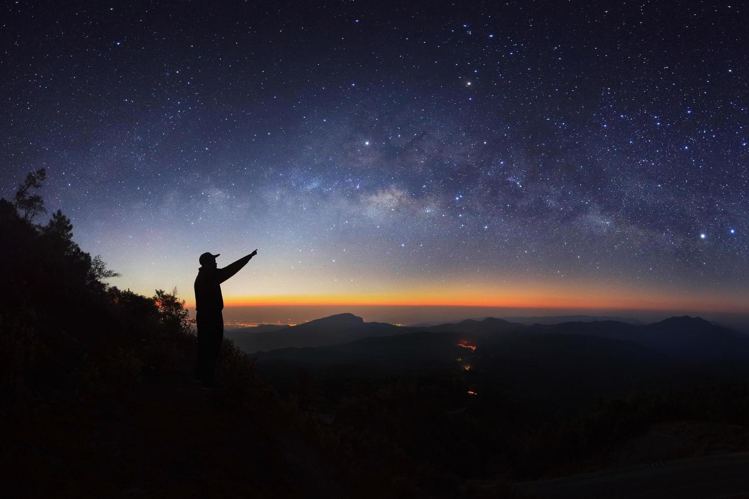 A Man is standing next to the milky way galaxy pointing on a bright star at Doi inthanon Chiang mai, Thailand. photo