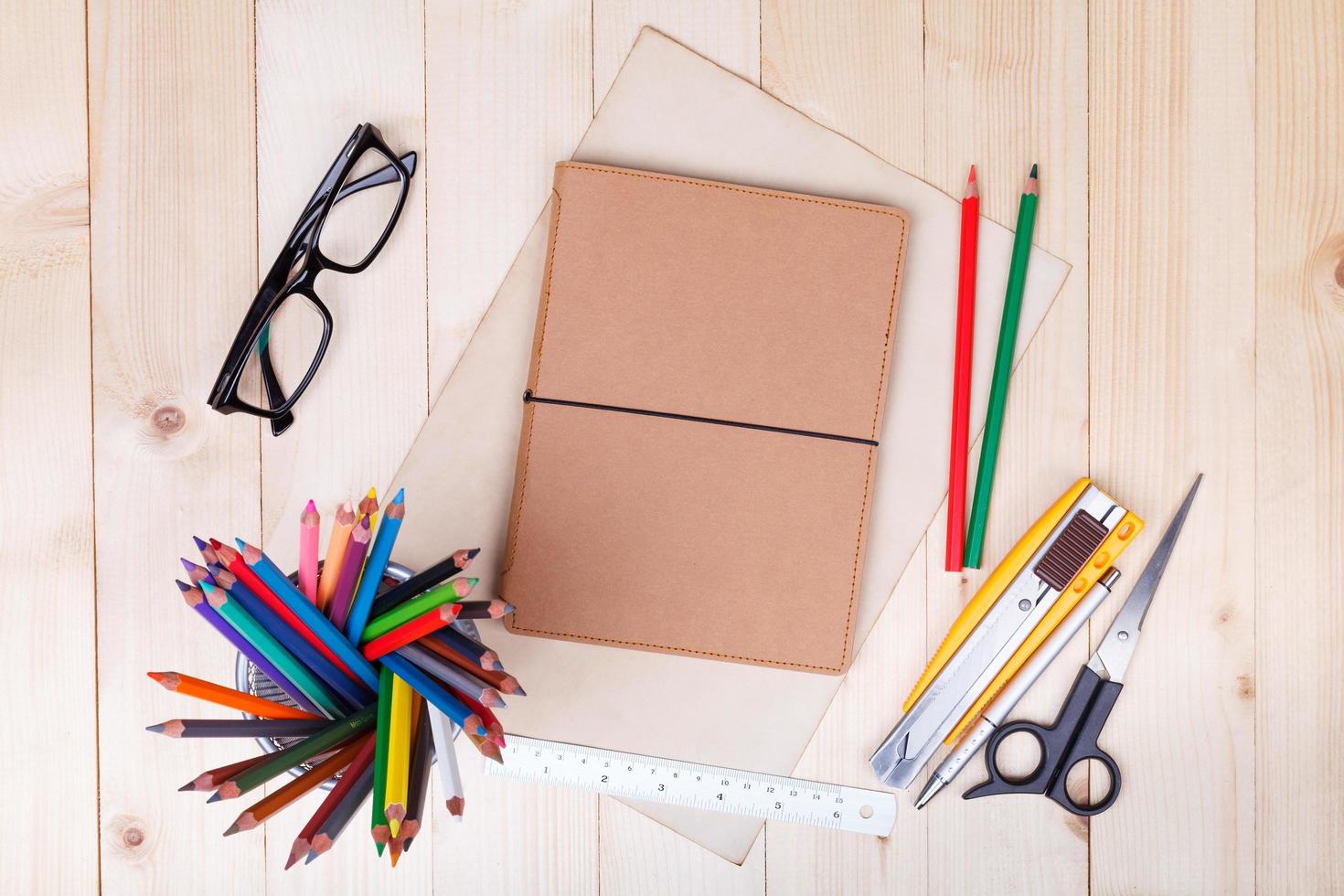 Workplace with colored pencils and supplies, notebook, eyeglass on wooden table photo