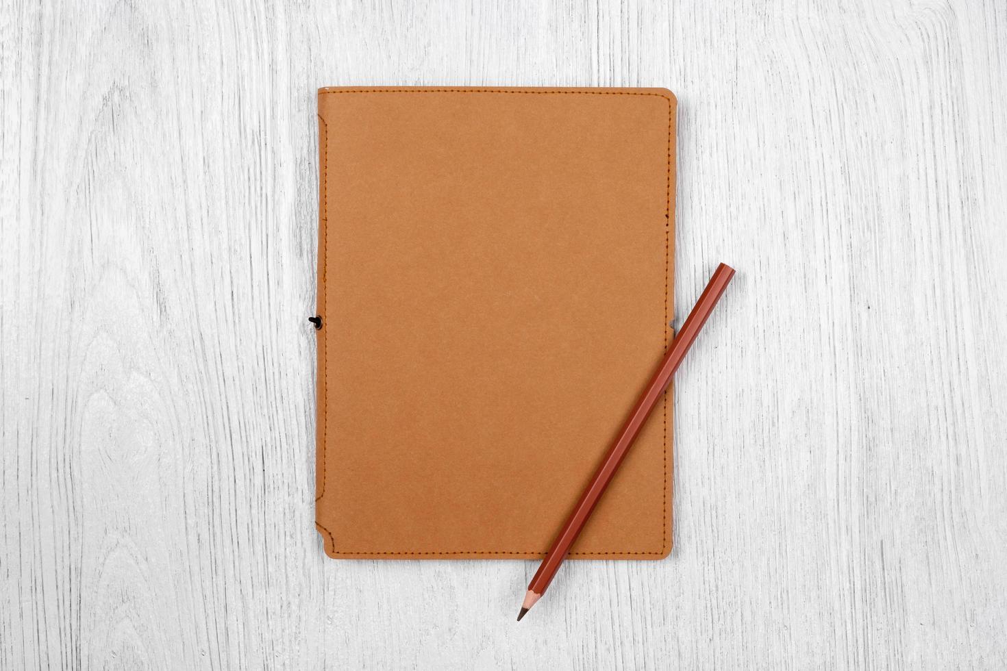 brown notebook and a pencil on white wooden table, top view photo