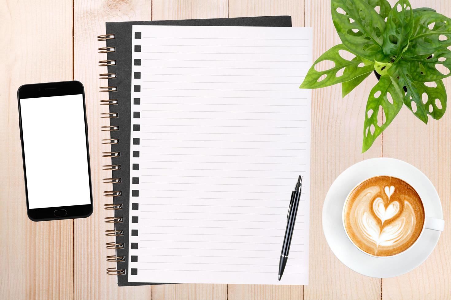 An open blank notebook, smartphone with pen and a cup of latte coffee on wooden table. photo