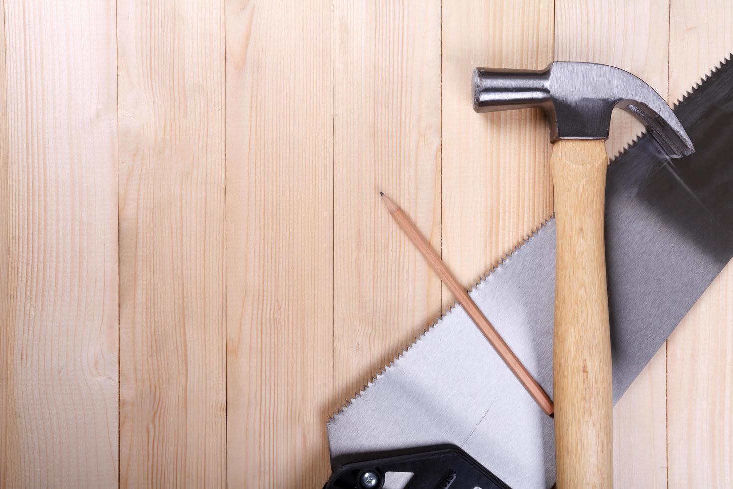 handsaw, claw hammer and pencil on wooden desk background photo