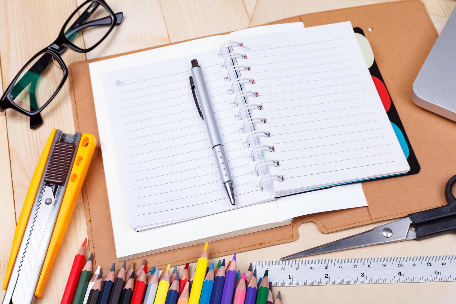 Workplace with colored pencils and supplies, laptop, notebook, eyeglass on wooden table photo