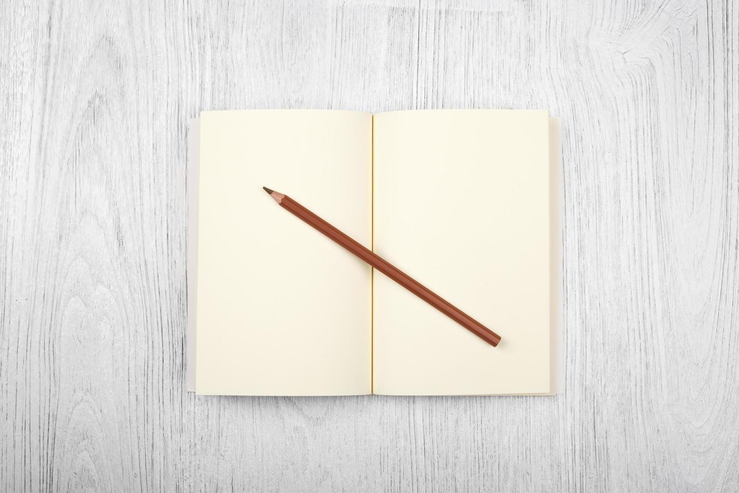 Open brown notebook and a pencil on white wooden table, top view photo