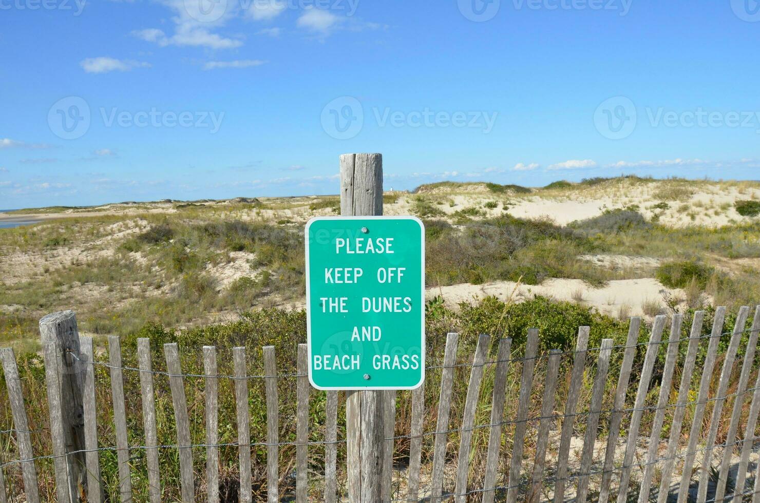 Valla de madera y dunas de arena en la playa con el cartel de por favor manténgase alejado foto