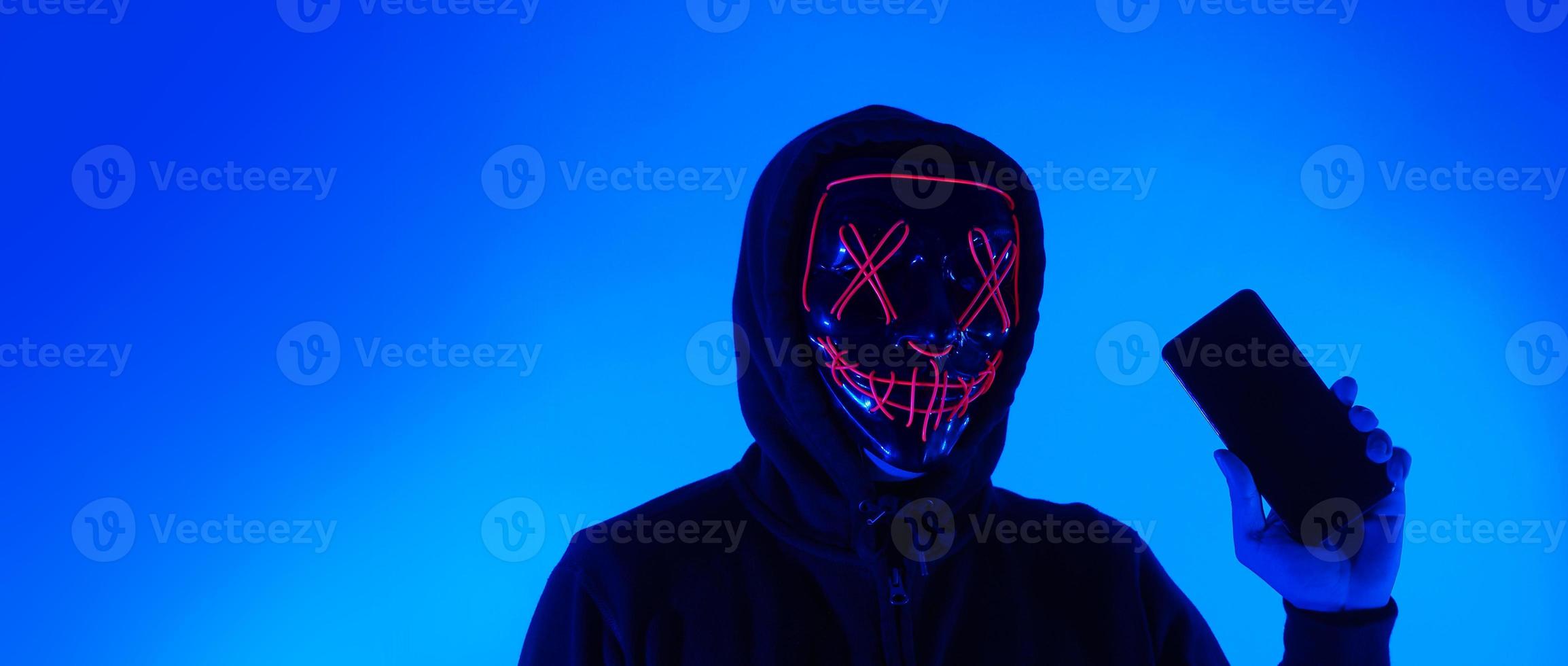 Anonymous hacker and face mask with smartphone in hand. photo