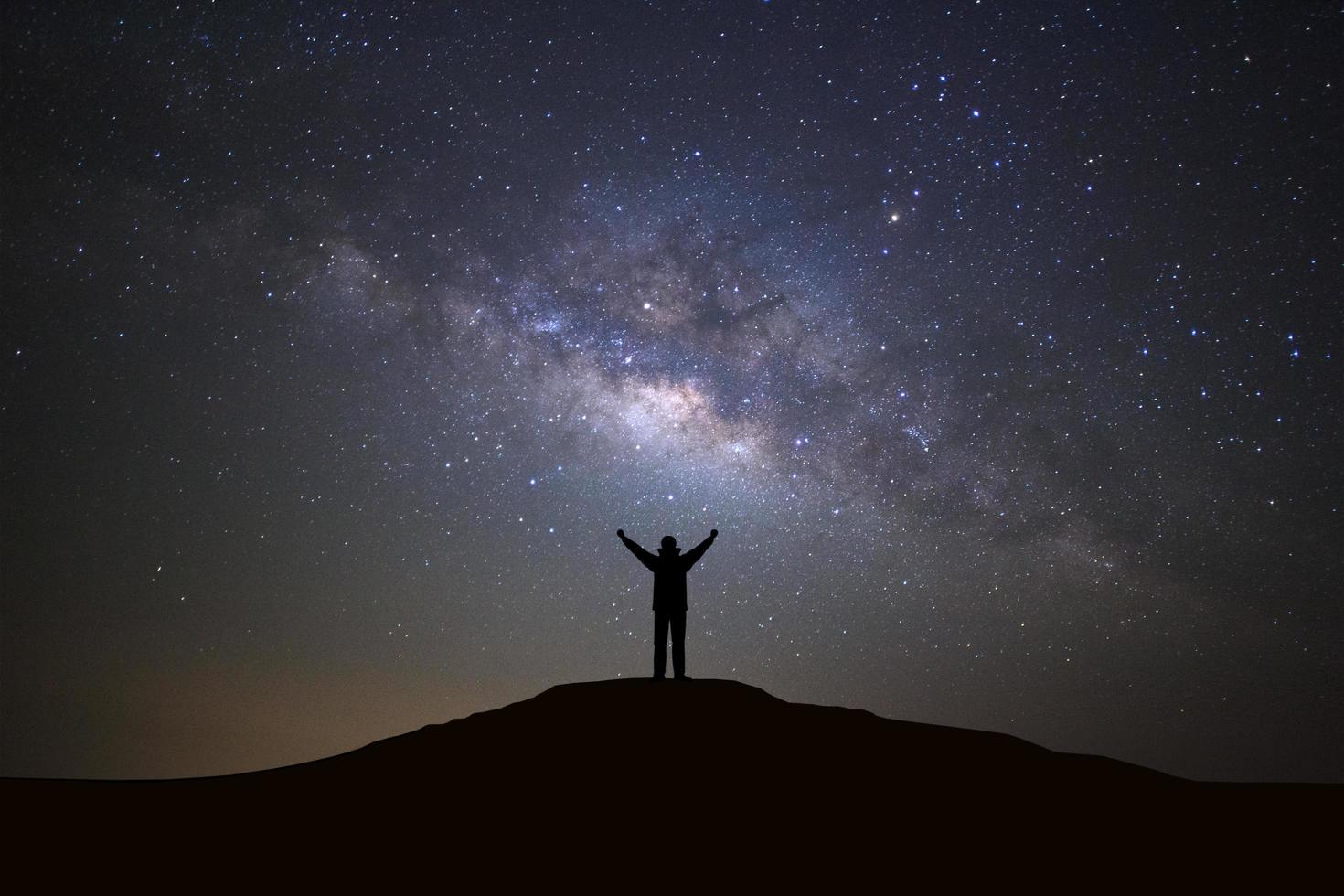 Landscape with milky way galaxy, Starry night sky with stars and silhouette of a standing sporty man with raised up arms on high mountain. photo