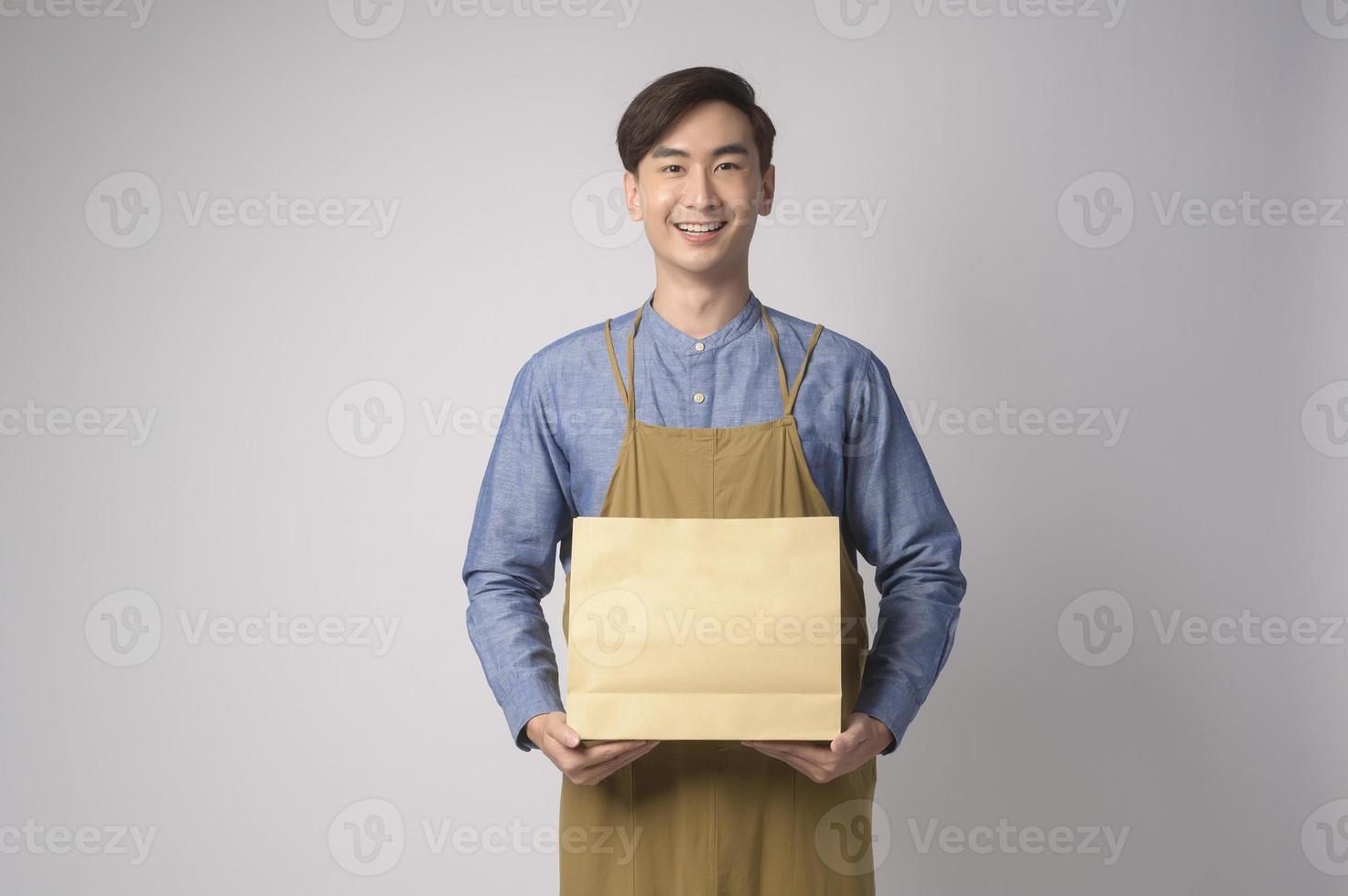 Portrait of young asian man wearing apron holding paper bag over white background studio, Save earth concept. photo