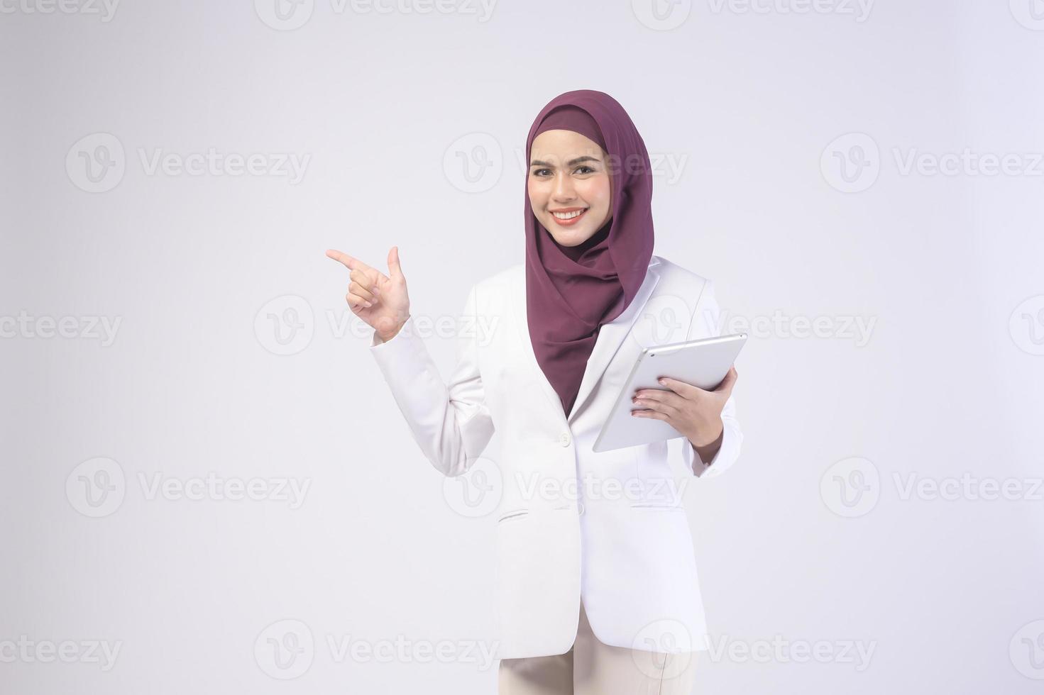 hermosa mujer de negocios musulmana con traje blanco con hiyab sosteniendo una tableta en el estudio foto