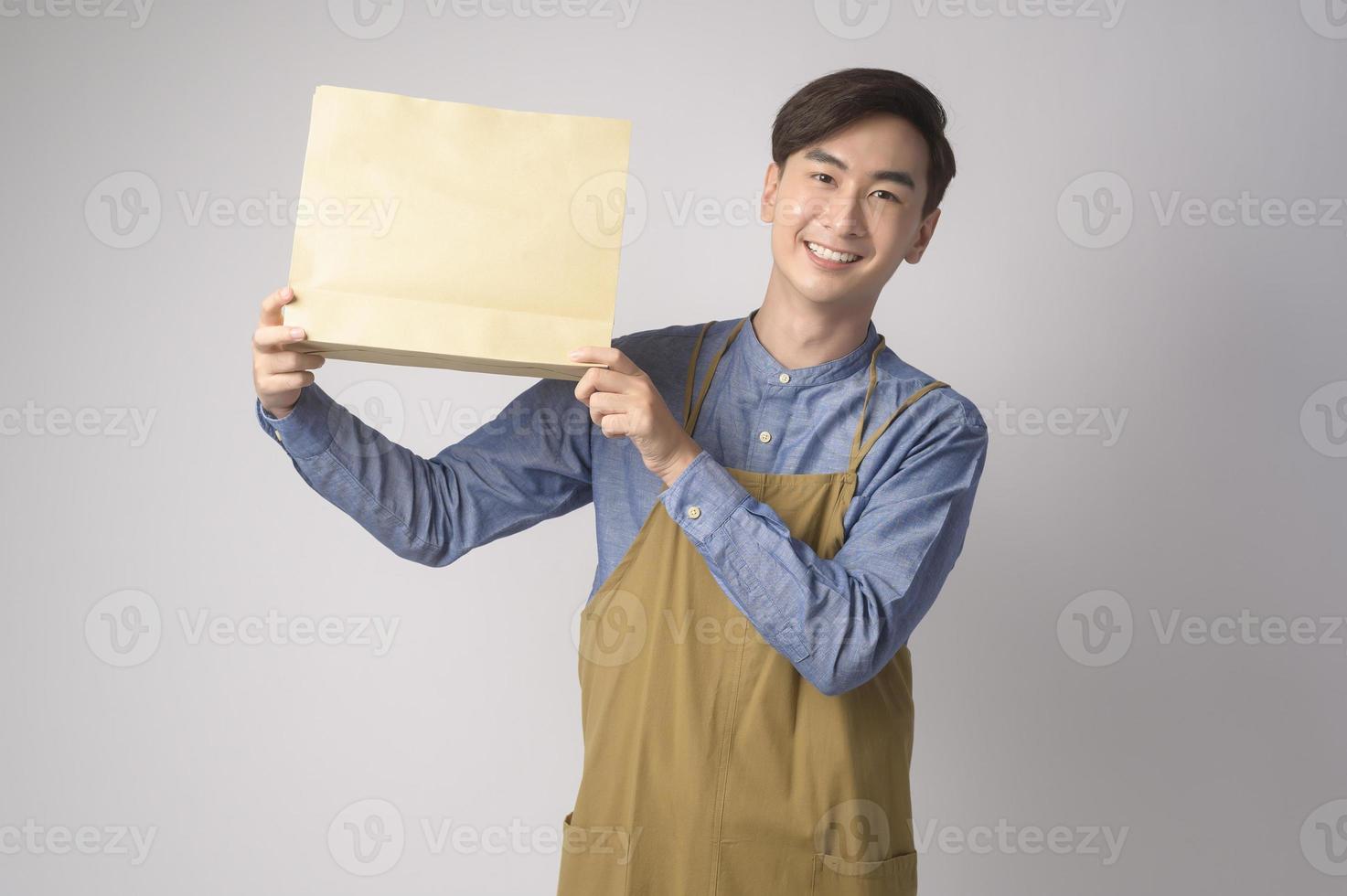 Portrait of young asian man wearing apron holding paper bag over white background studio, Save earth concept. photo