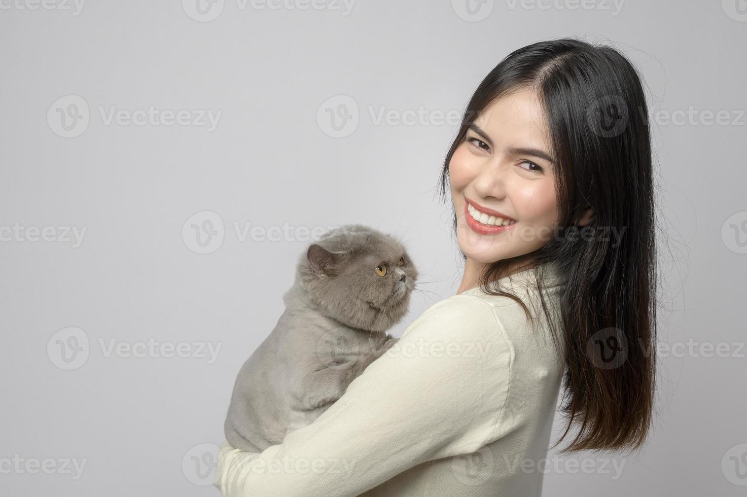 una mujer joven está sosteniendo un gato adorable, jugando con un gato en un estudio de fondo blanco foto