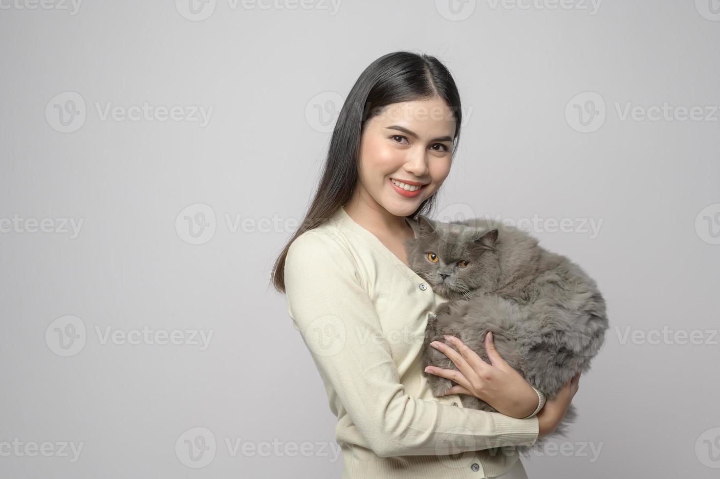 una mujer joven está sosteniendo un gato adorable, jugando con un gato en un estudio de fondo blanco foto