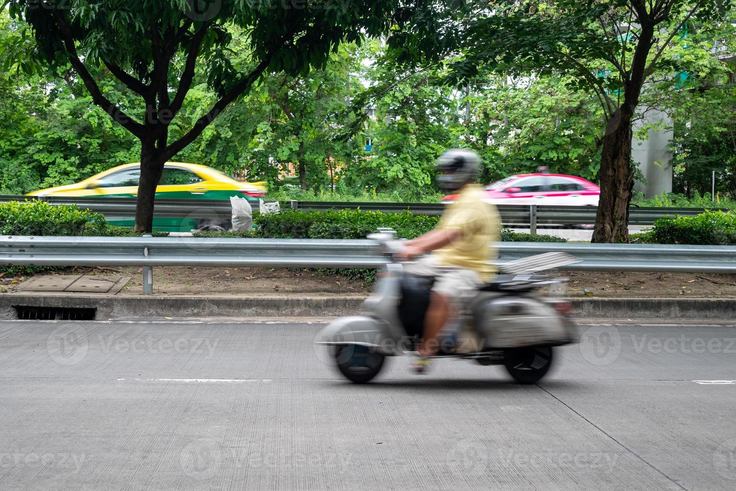 A man on motorbike moving fast, blurred motion. Biker ride along the road in green urban area. photo