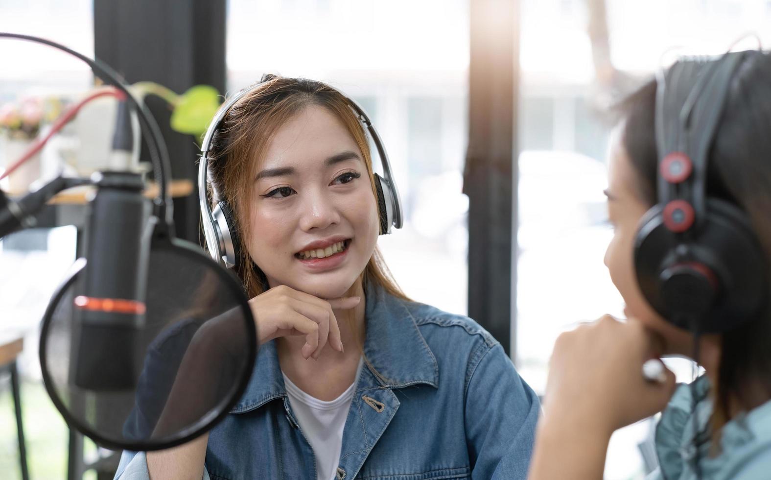 Smile two asian young woman, man radio hosts in headphones, microphone while talk, conversation, recording podcast in broadcasting at studio together. Technology of making record audio concept. photo