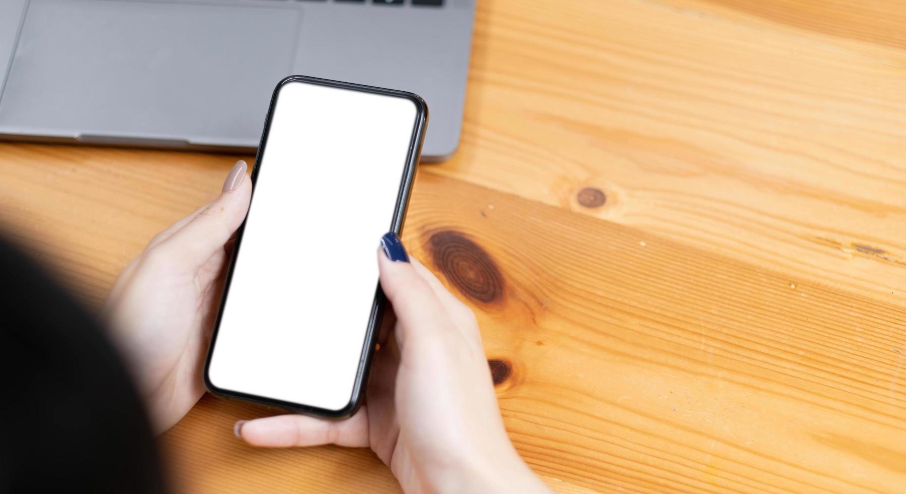 hand woman using a telephone, empty screen smart phone and computer on wooden table top view. photo