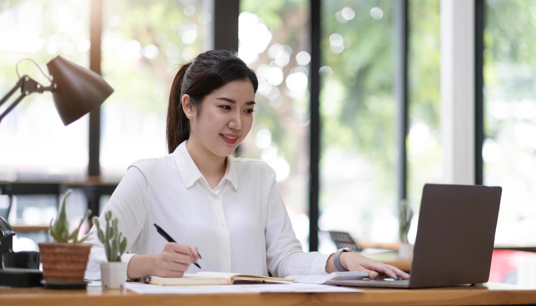 Beautiful young asian woman sitting at coffee shop using laptop. Happy young businesswoman sitting at table in cafe with tab top computer. photo