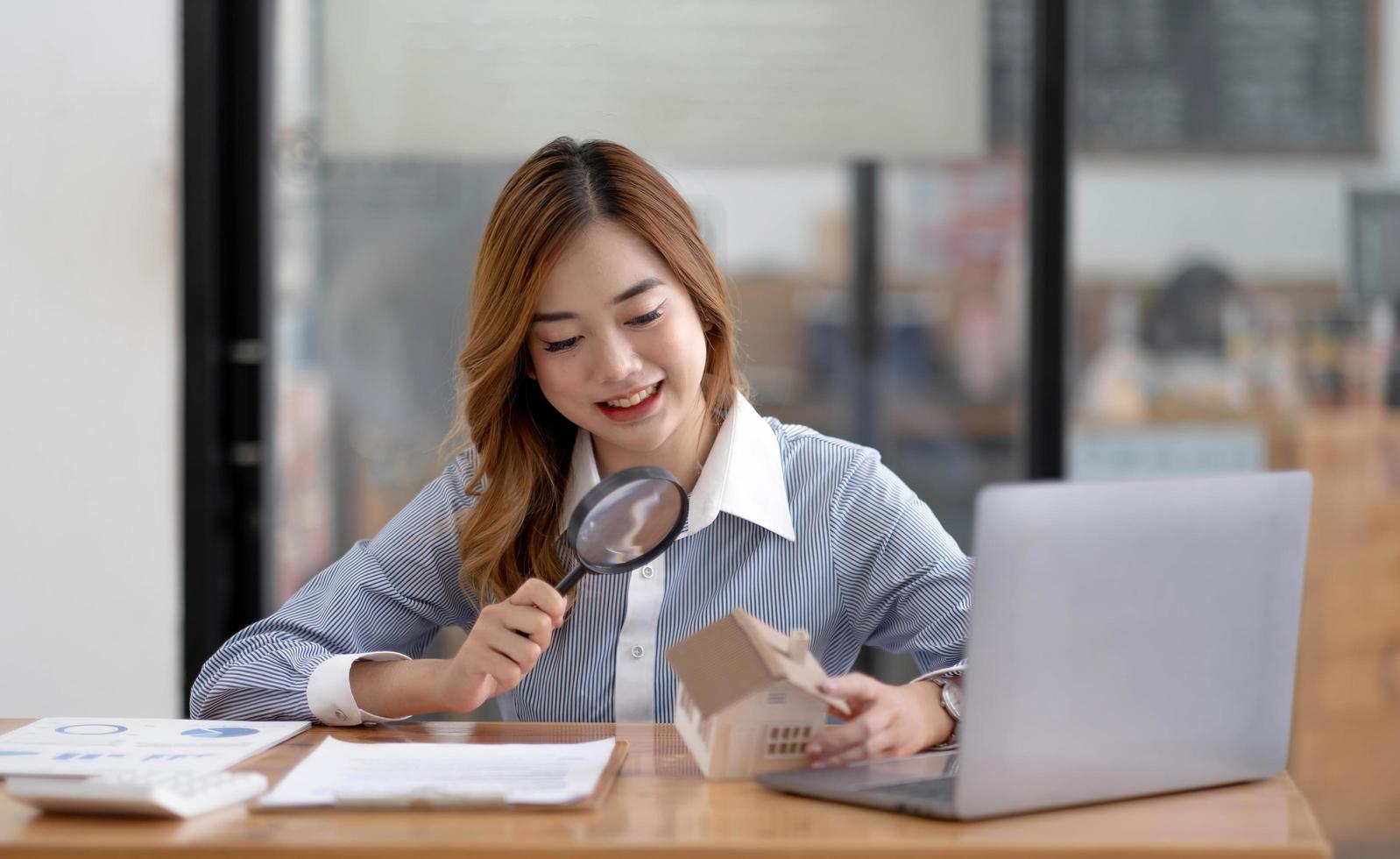 primer plano de mujeres de negocios que sostienen una lupa que encuentra una forma de madera de una casa, agente inmobiliario, agente, seguro, desarrollador, planificación e inversión concepto de negocio inmobiliario, foto