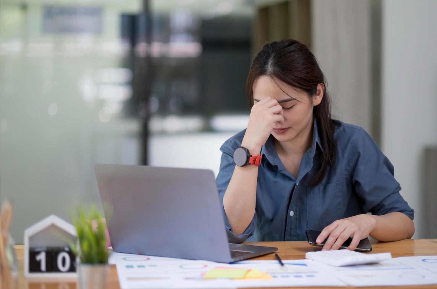 Asian women sitting in a home office With stress and eye strain.Tired businesswoman holding eyeglasses and massaging nose bridge. There are tablets, laptops, and coffee. photo
