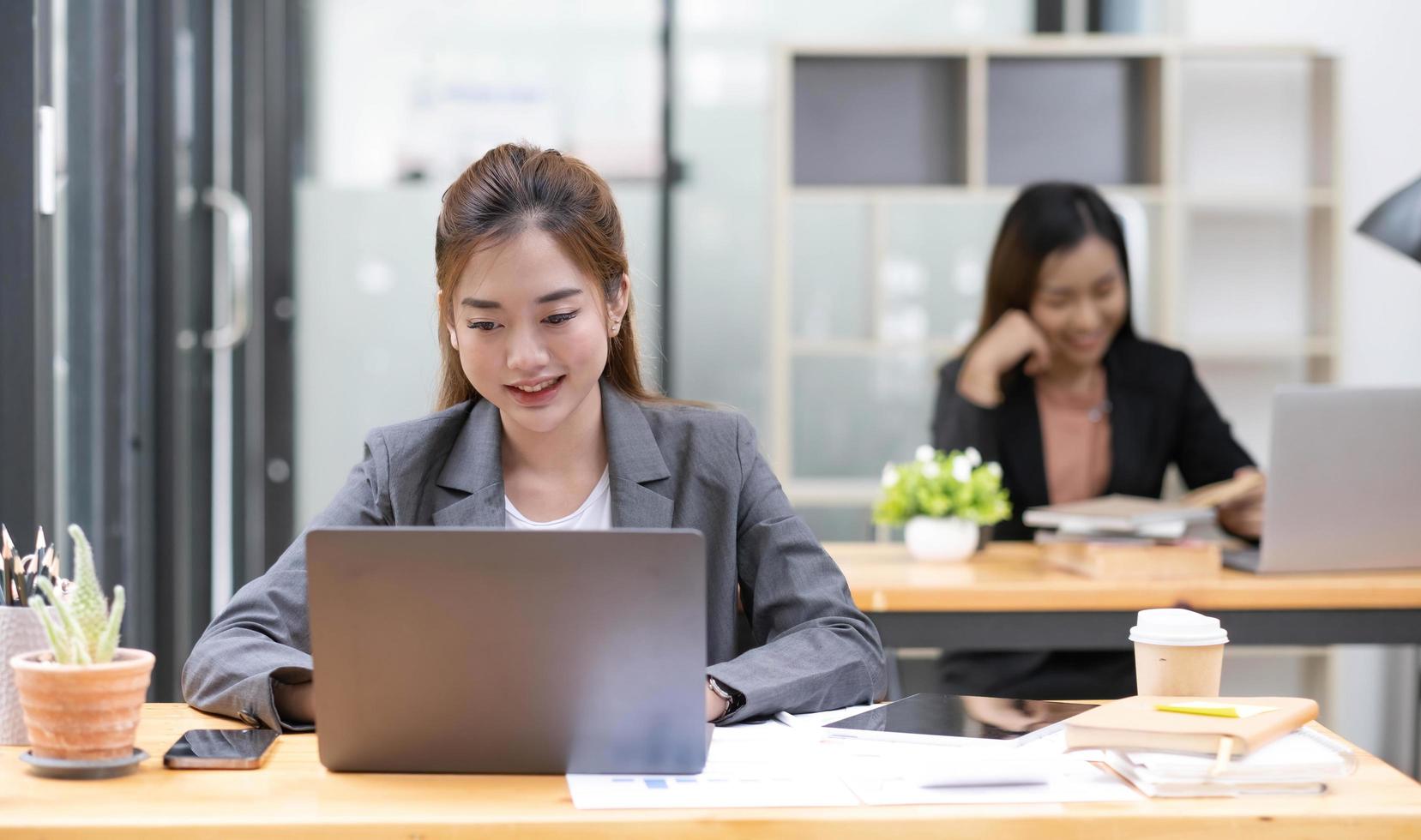 Two business women are working on a notebook computer, holding a pen and looking at the screen in office. photo
