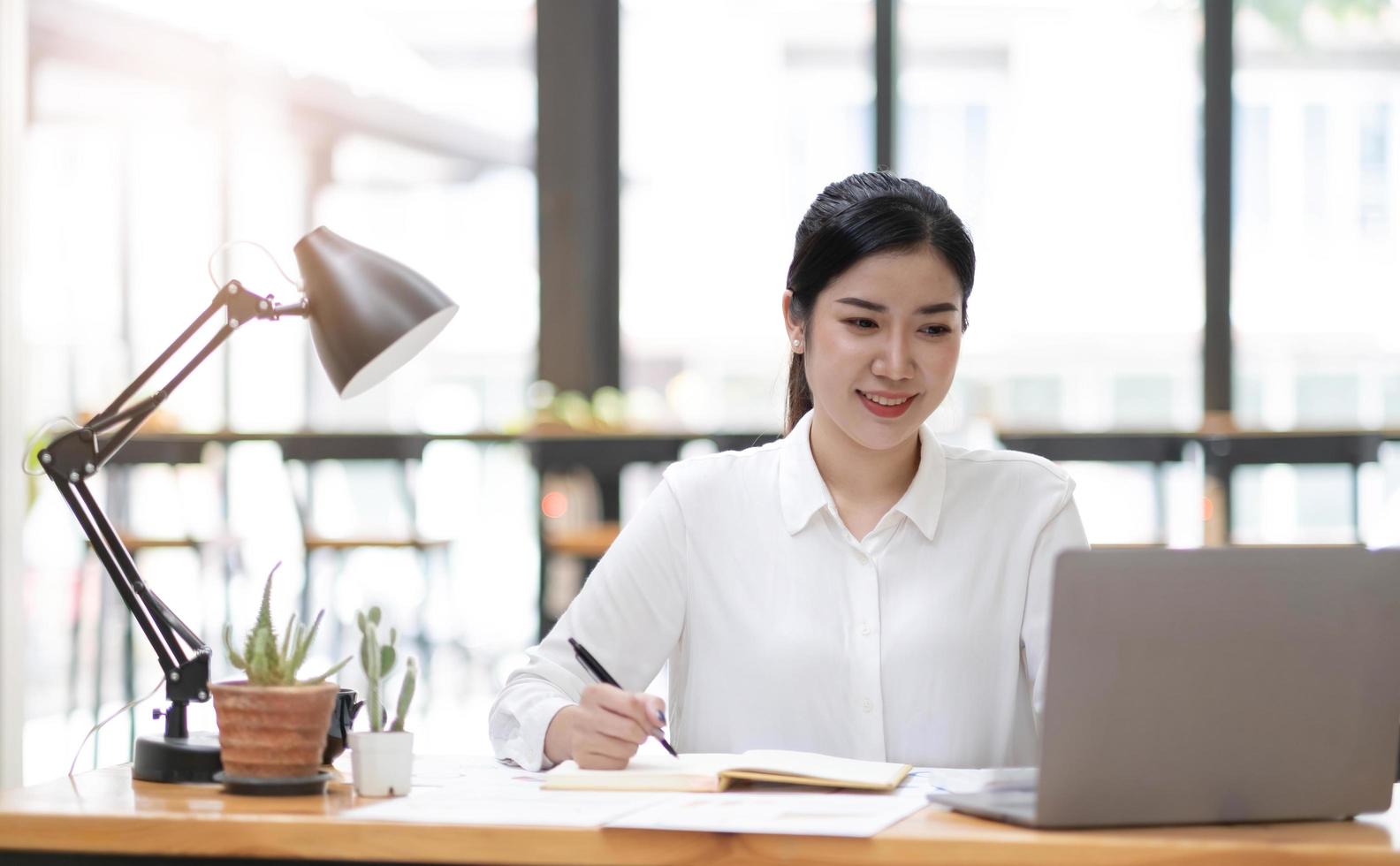 Beautiful young asian woman sitting at coffee shop using laptop. Happy young businesswoman sitting at table in cafe with tab top computer. photo