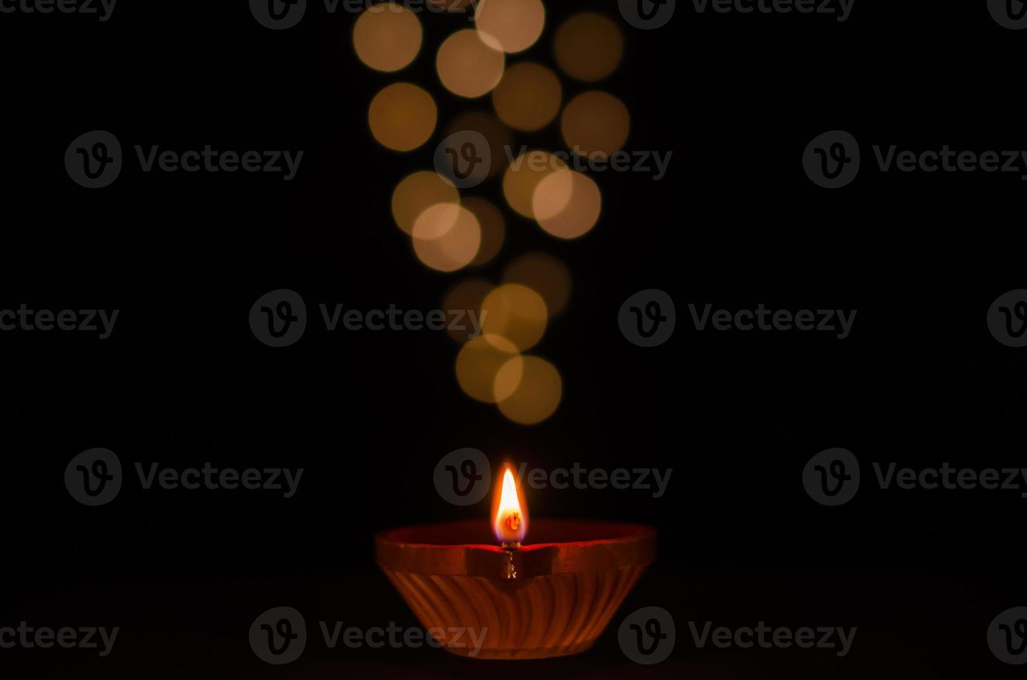 Selective focus on flame of clay diya lamp lit on dark background with bokeh lights. Diwali festival concept. photo