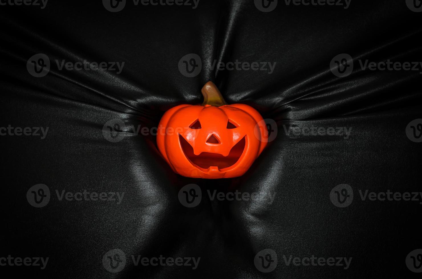 Halloween pumpkin holding by hand pressing through black fabric background. Halloween festival concept. photo