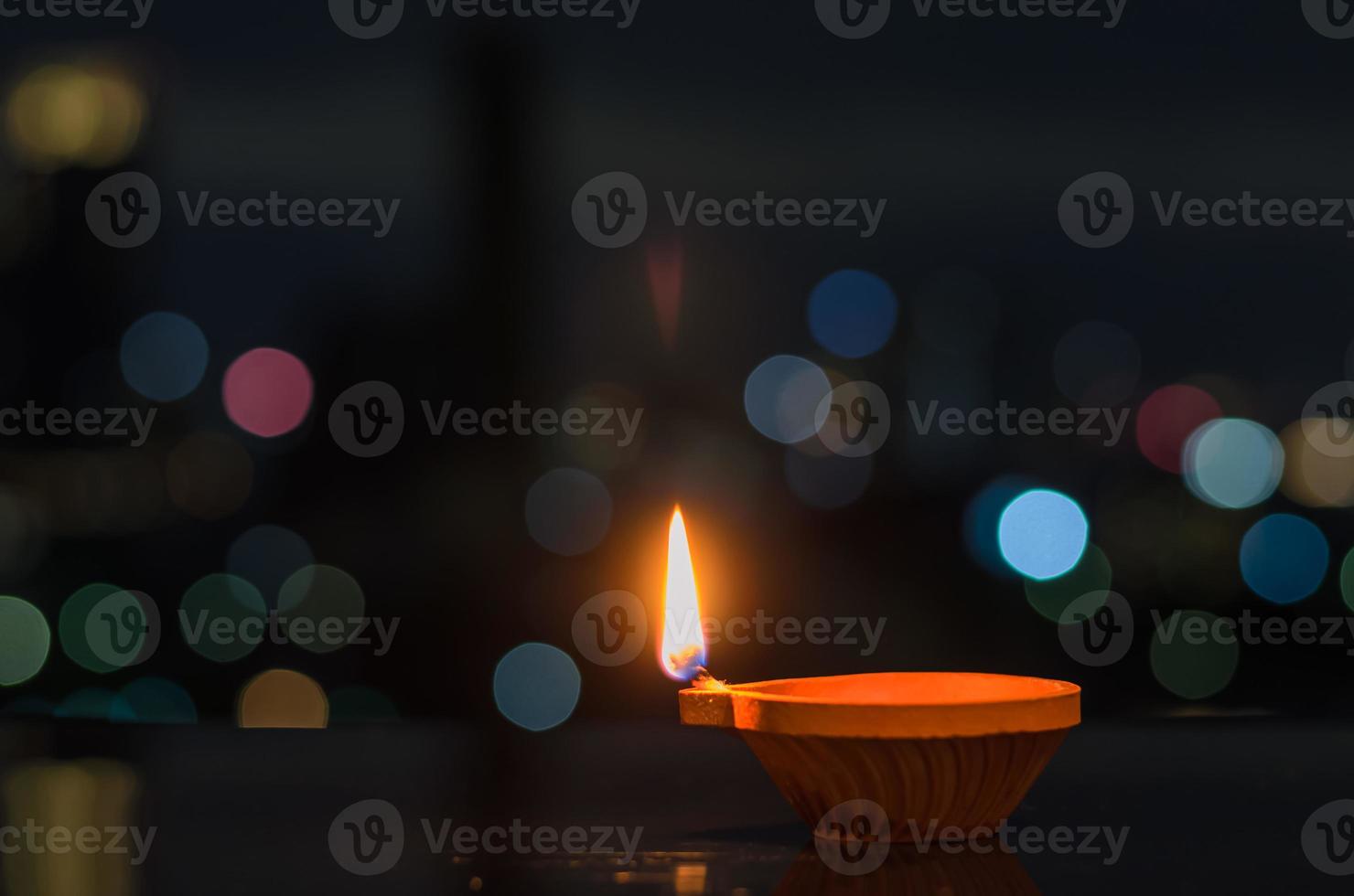 Selective focus on the flame of clay diya lamp with colorful city bokeh lights. Diwali festival concept. photo