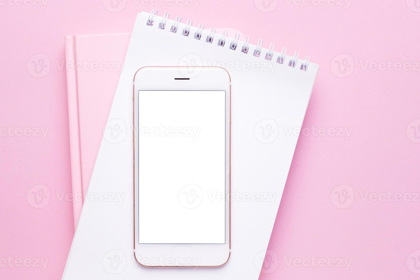 Mobile phone mock up and notebook on pink pastel table top view in flat lay style. Woman working desk. photo
