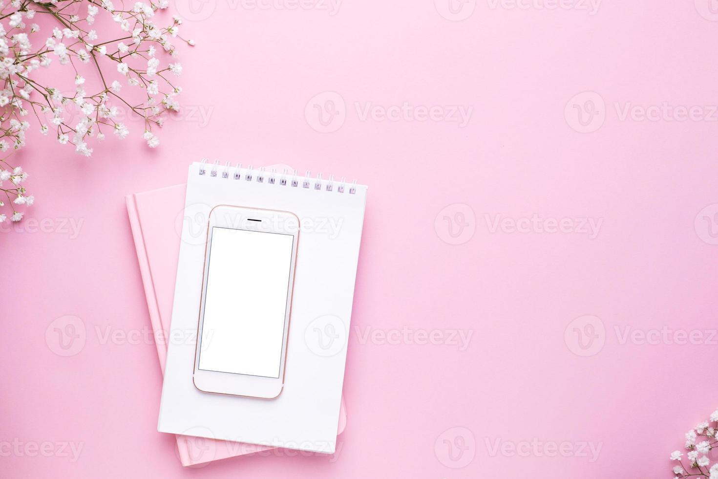 Mobile phone mock up and white flowers on pink pastel table top view in flat lay style. Woman working desk. photo