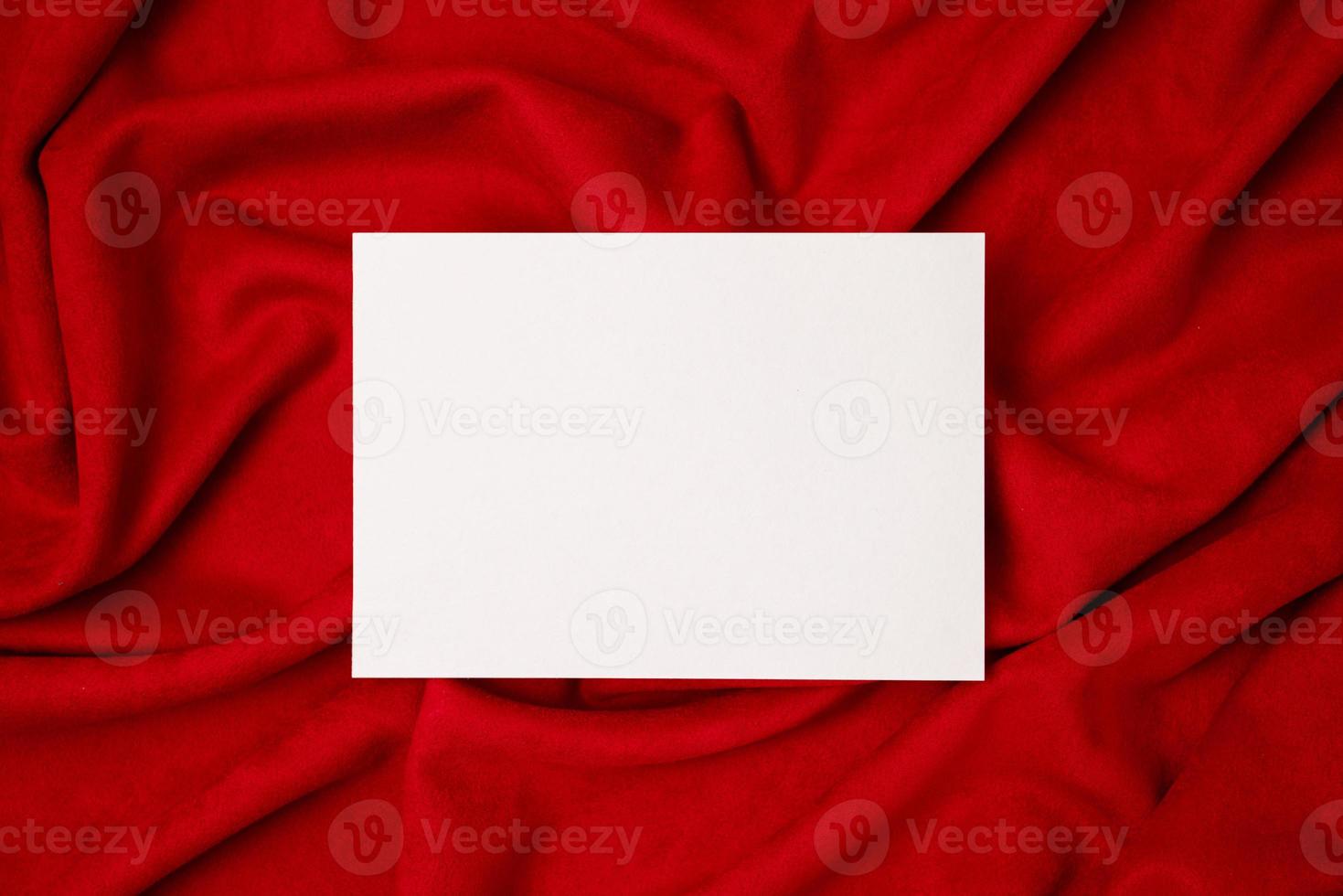 Blank white paper card on red fabric . Flat lay, top view, copy space. Wedding invitation card design. photo