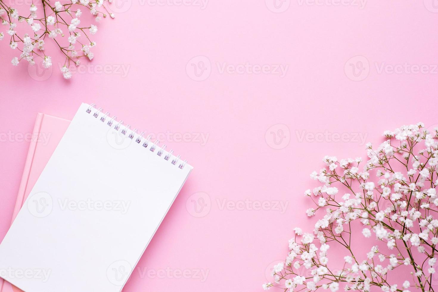 Empty notebook and white flowers on pink pastel table top view in flat