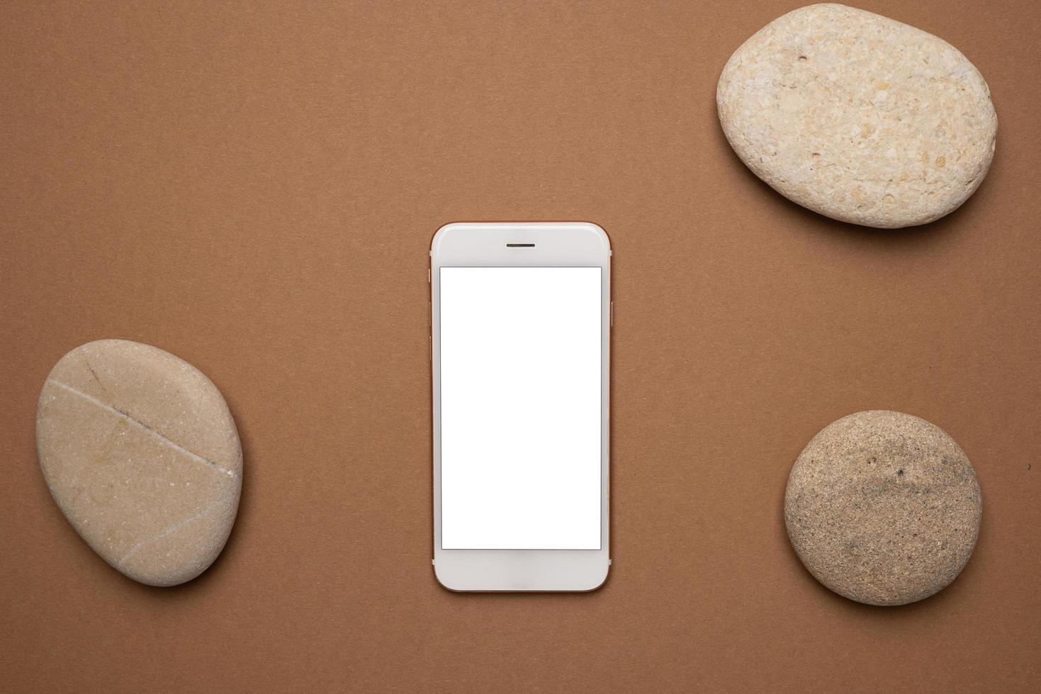 Mobile phone with white screen and stone on a light brown background. Trend, minimal concept with copyspace photo