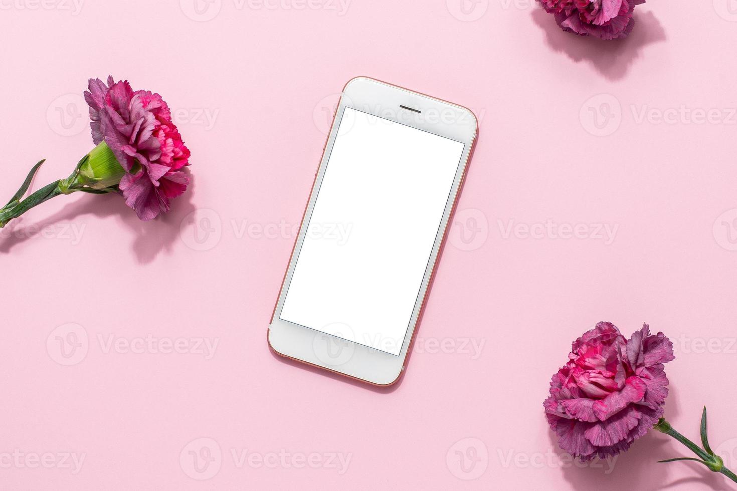 Mobile phone mock up and pink flowers on pink pastel table top view in flat lay style. Woman working desk.Spring colour photo