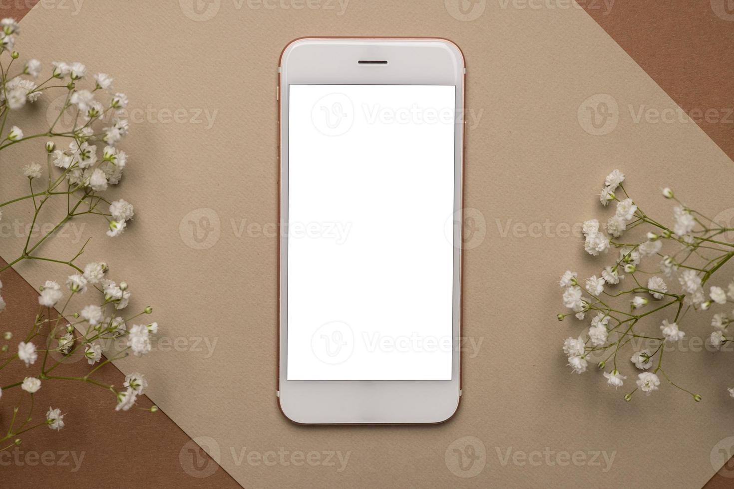 Mobile phone with white screen and dry flower branch and stone on a light brown background. Trend, minimal concept with copyspace photo