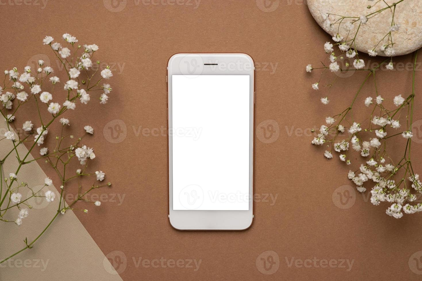 Mobile phone with white screen and dry flower branch and stone on a light brown background. Trend, minimal concept with copyspace photo