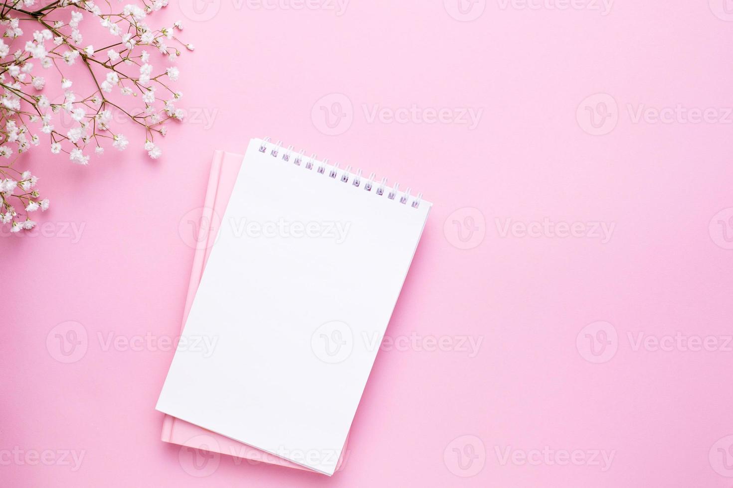 Empty notebook and white flowers on pink pastel table top view in flat lay style. Woman working desk. photo