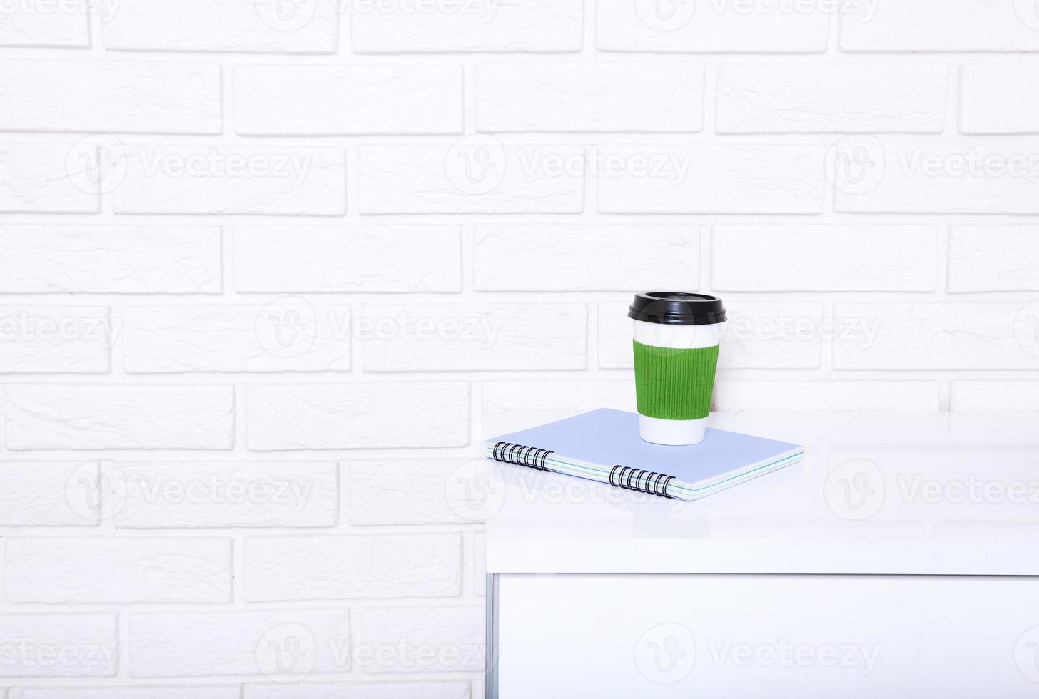 Stylish macro cup of coffee and notebook in office. Selective focus and copy space. Brick wall and workplace business concept. photo