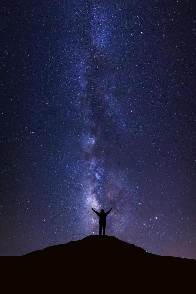 paisaje con vía láctea, cielo nocturno con estrellas y silueta de hombre parado en alta montaña foto