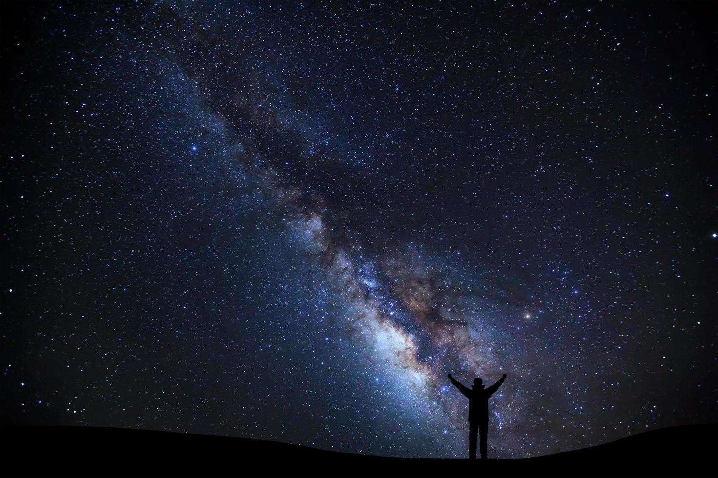 landscape with milky way, Night sky with stars and silhouette of a standing sporty man with raised up arms on high mountain. photo