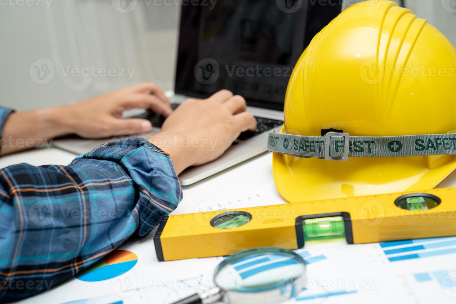 Asian engineer with architectural house plan project blueprint, graph and yellow helmet and engineering construction tools. photo