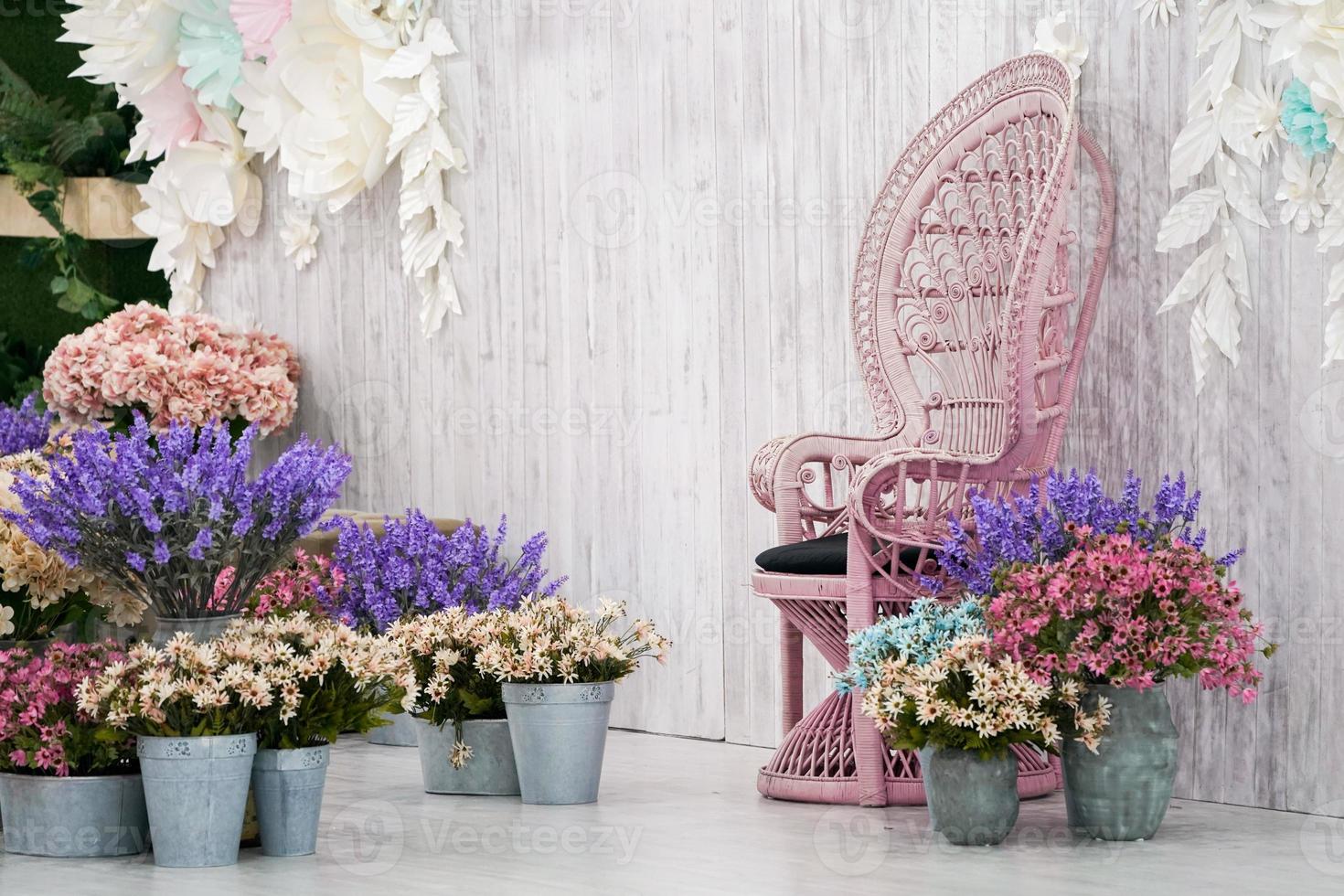 lujosa silla de bambú vintage frente a un fondo de madera blanca y muchas flores alrededor. foto