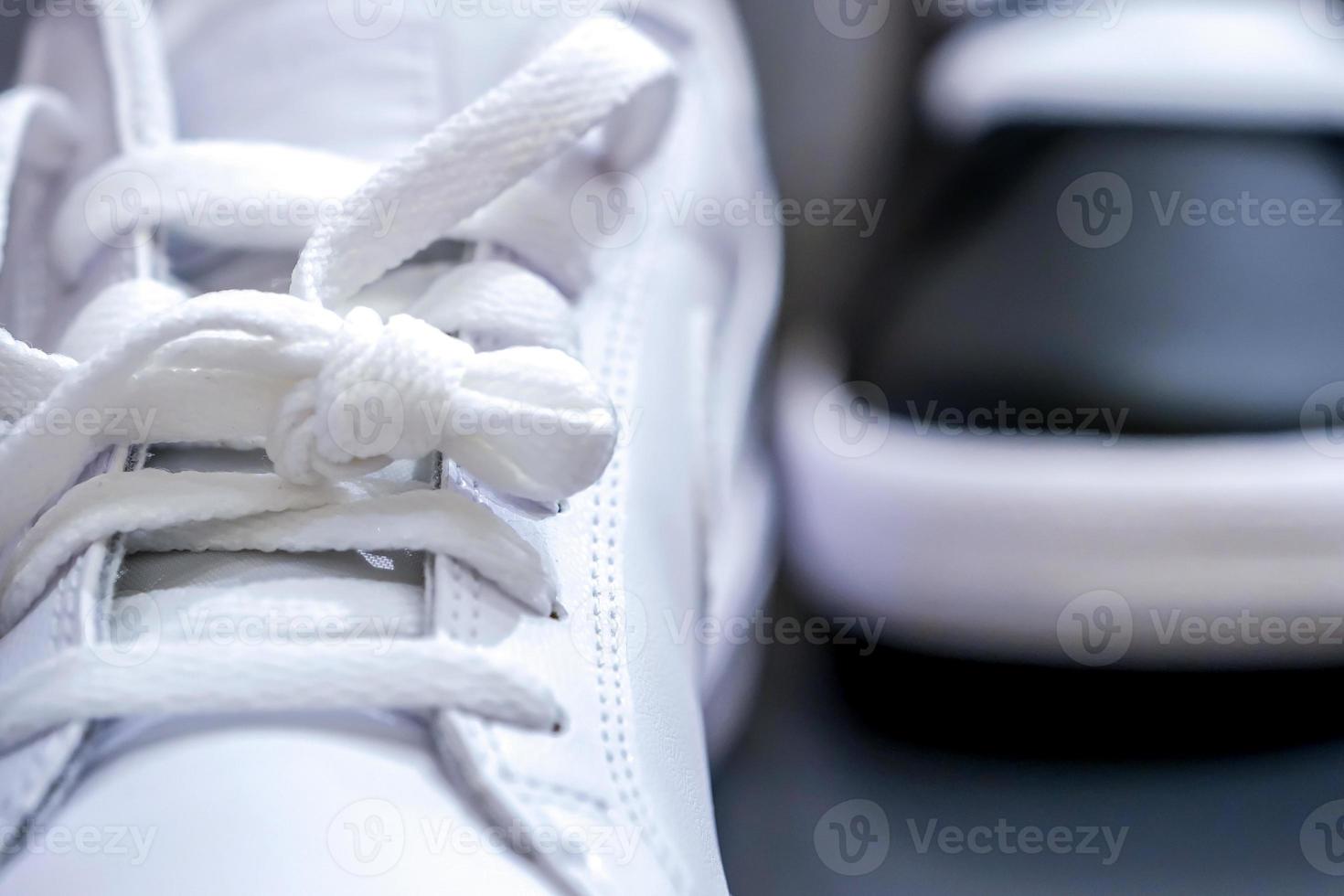 Cierre los cordones de las zapatillas de moda blancas con zapatos negros en el fondo. foto