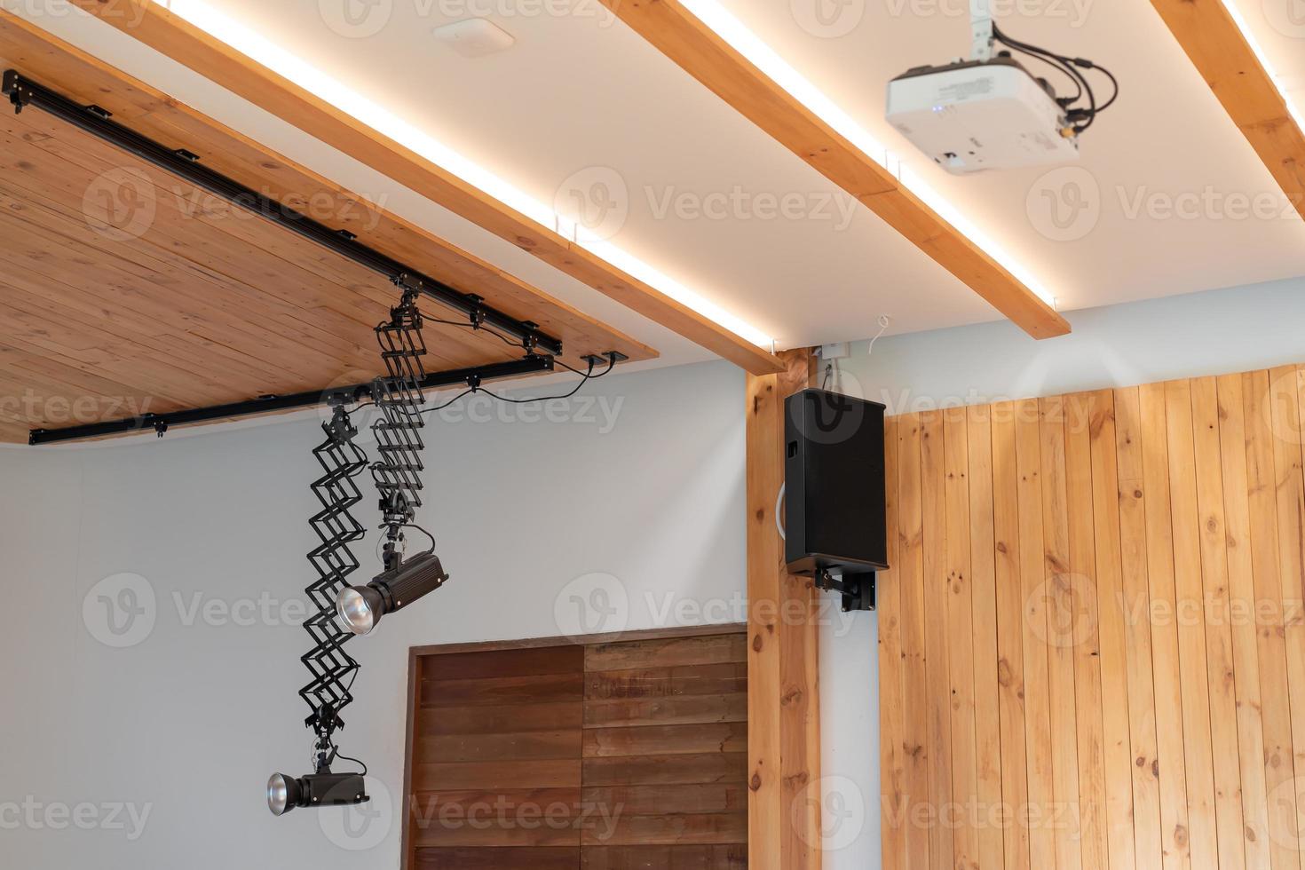 The Equipment of Seminar room Black 2 Spotlights, speaker, and white projector are hanged on to ceiling and wall in the hall. photo