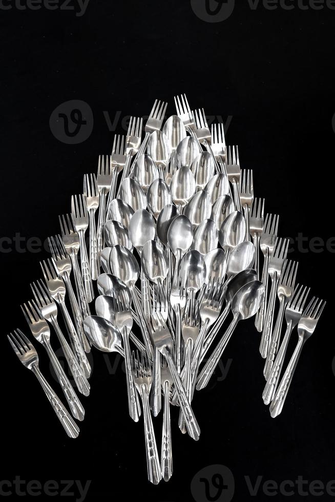 topview of Spoons and forks are arranged on the black cloth background. photo