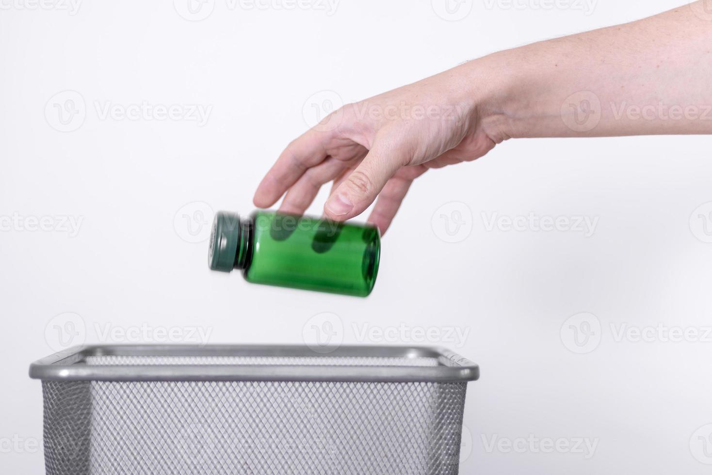 la mano tira una pequeña botella de plástico a la basura. foto