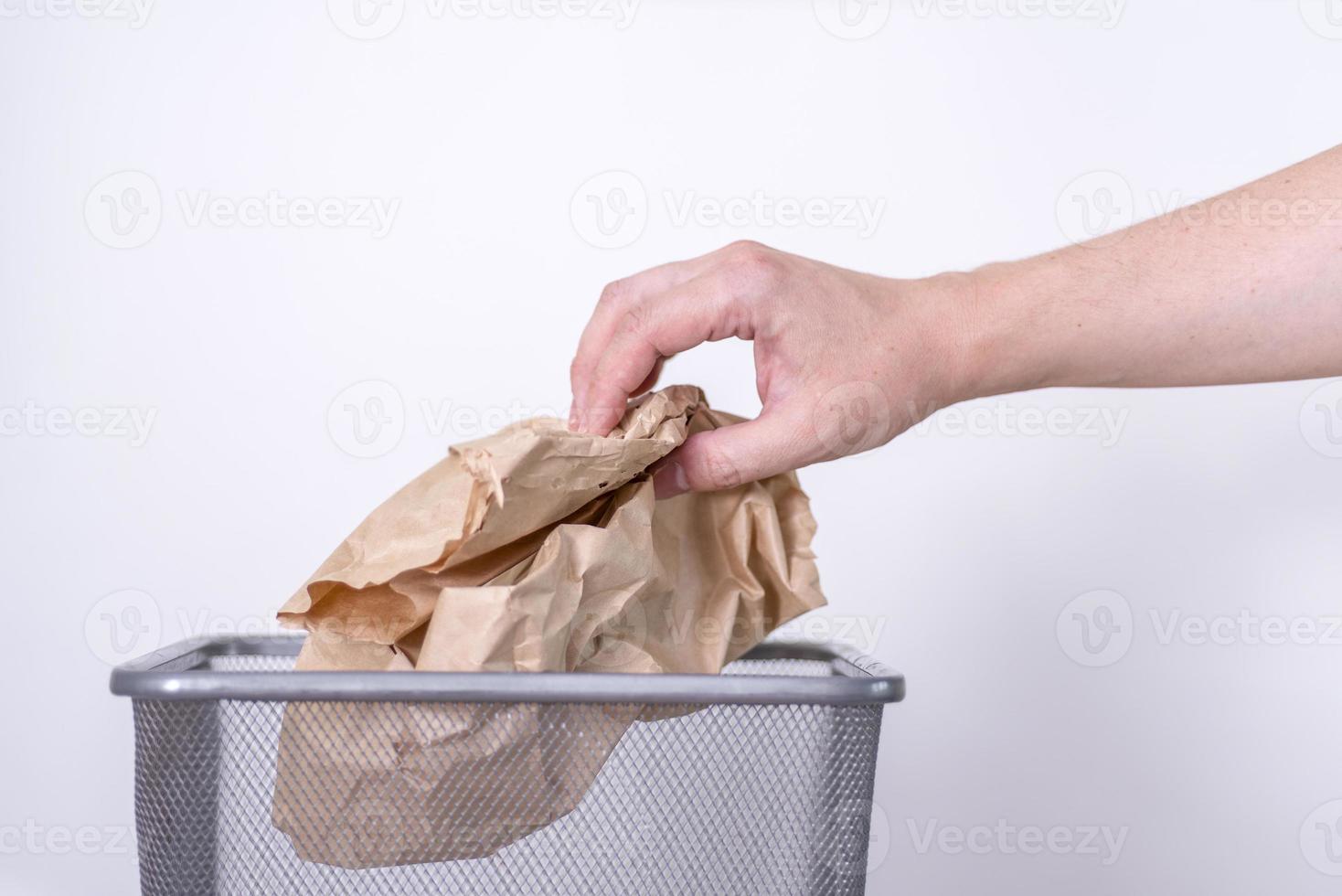 A hand throws a crumpled paper bag into a trash can. photo